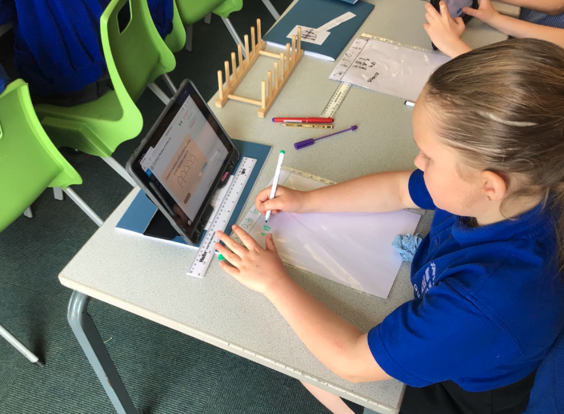 Primary student working on CENTURY on a tablet with a pen and whiteboard