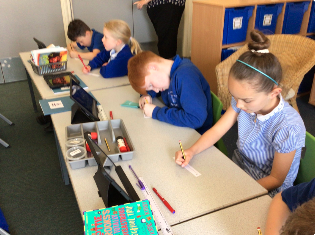 Primary student working on the CENTURY platform on a tablet and using pen and paper to complete a Your Turn